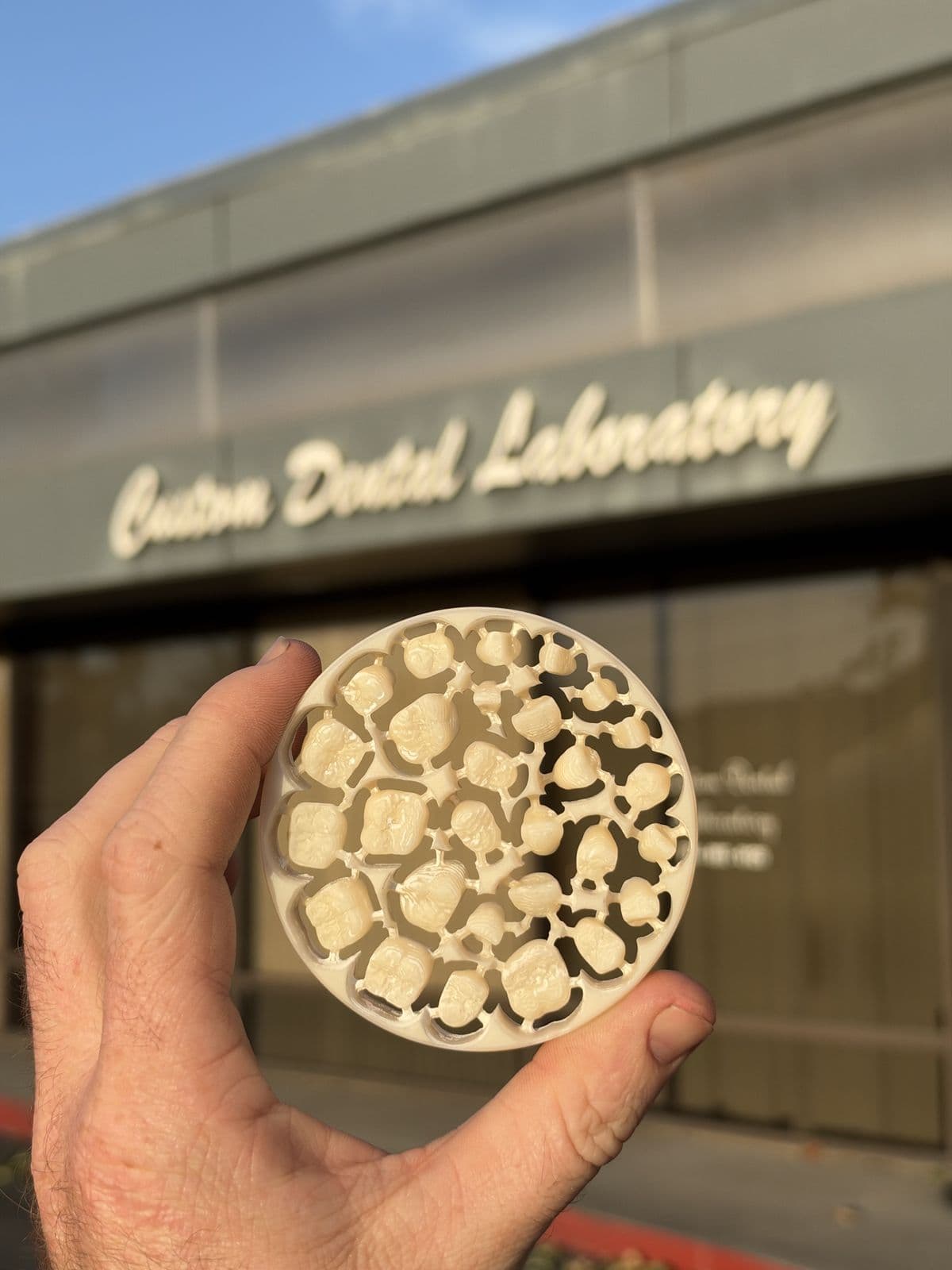 Freshly milled zirconia disc of crowns held up outside the Custom Dental Laboratory building